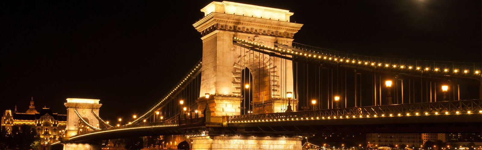 the chain bridge with the gresham palace and danube river in budapest at full moon - hungary at night